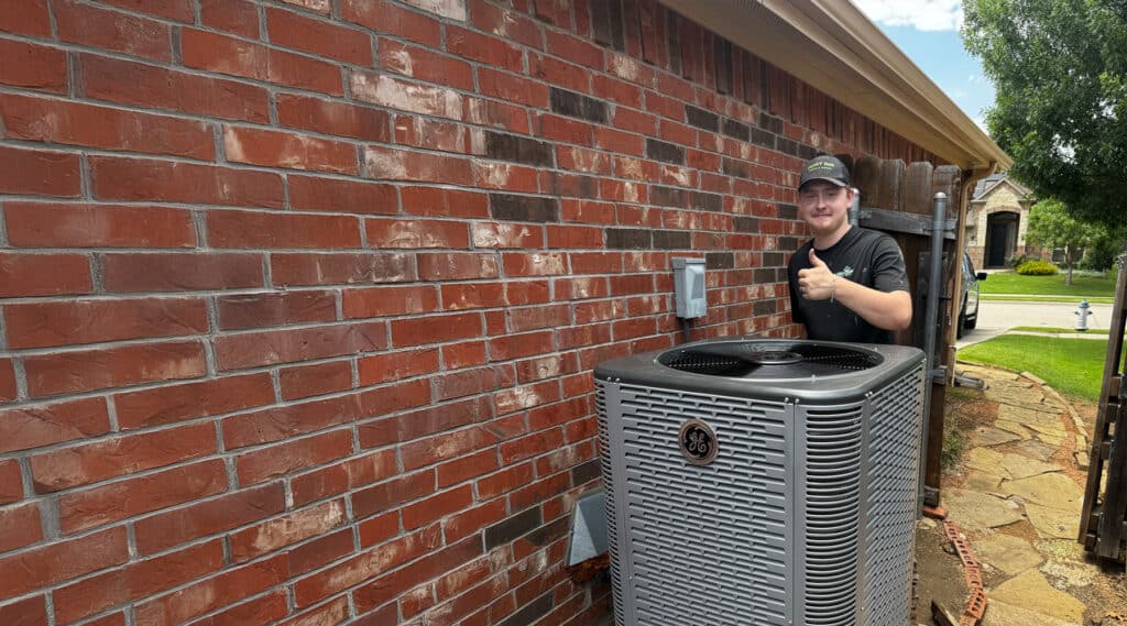 Happy technician giving a thumbs up next to an air conditioning unit.