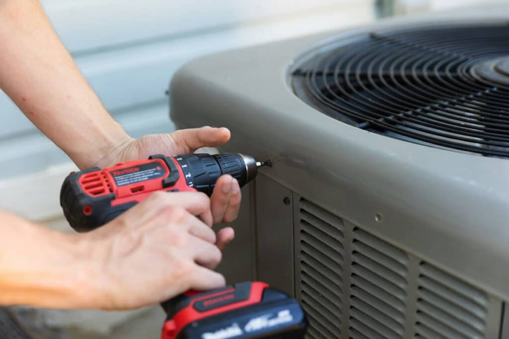 HVAC tech using a power drill to repair an air conditioning unit.