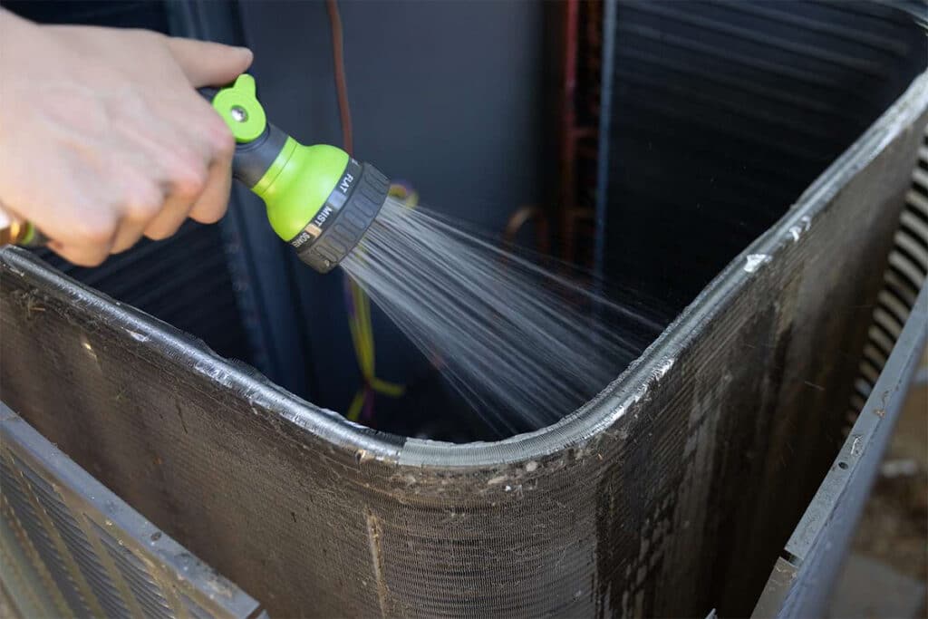 HVAC tech cleaning an air conditioner coil with a garden hose.