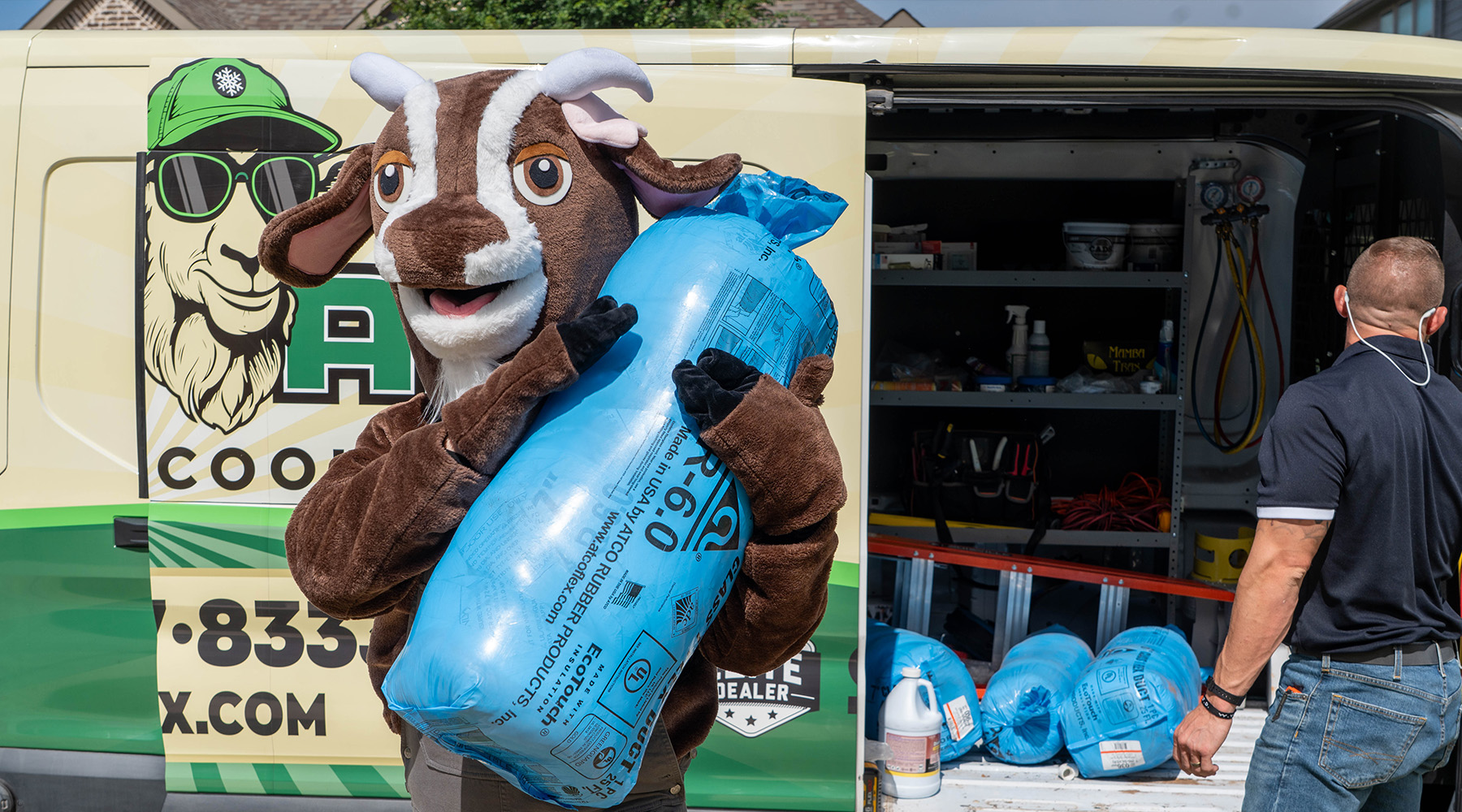 he Goat Air costumed mascot holding a large roll of blue EcoTouch R-6 flex duct insulation in front of the branded service van while a technician unloads more materials.