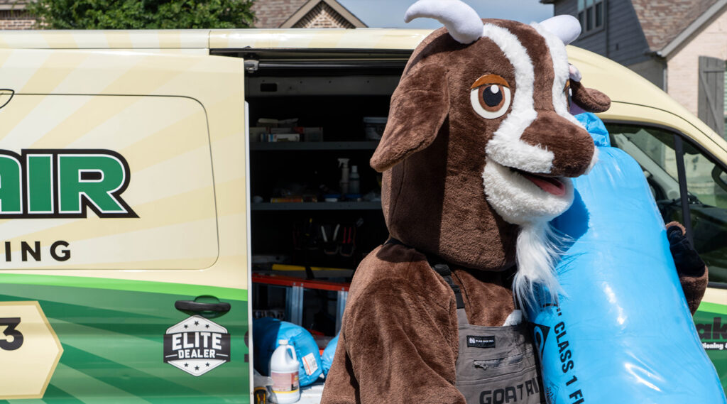 The Goat Air costumed mascot carrying a roll of blue R-6 flex duct insulation from the back of the branded Goat Air Elite Dealer service van.