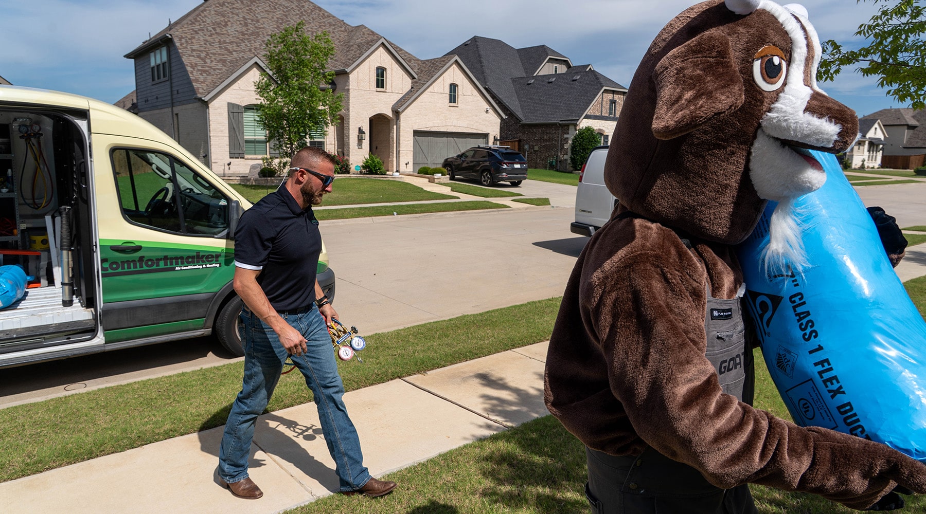 Goat Air technician carries refrigerant gauges while Gus the Goat hauls a bag of flex duct across a North Texas front lawn.